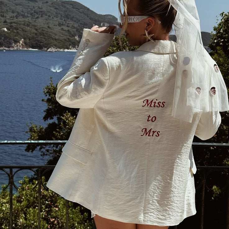 Person wearing a white bridal outfit with 'Miss to Mrs' text, standing by a scenic waterfront.