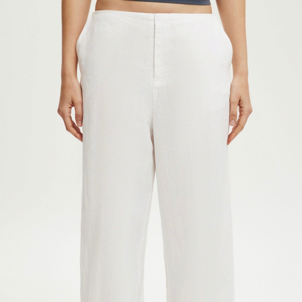 A person wearing high-waisted, wide-leg white trousers against a clean white studio background.