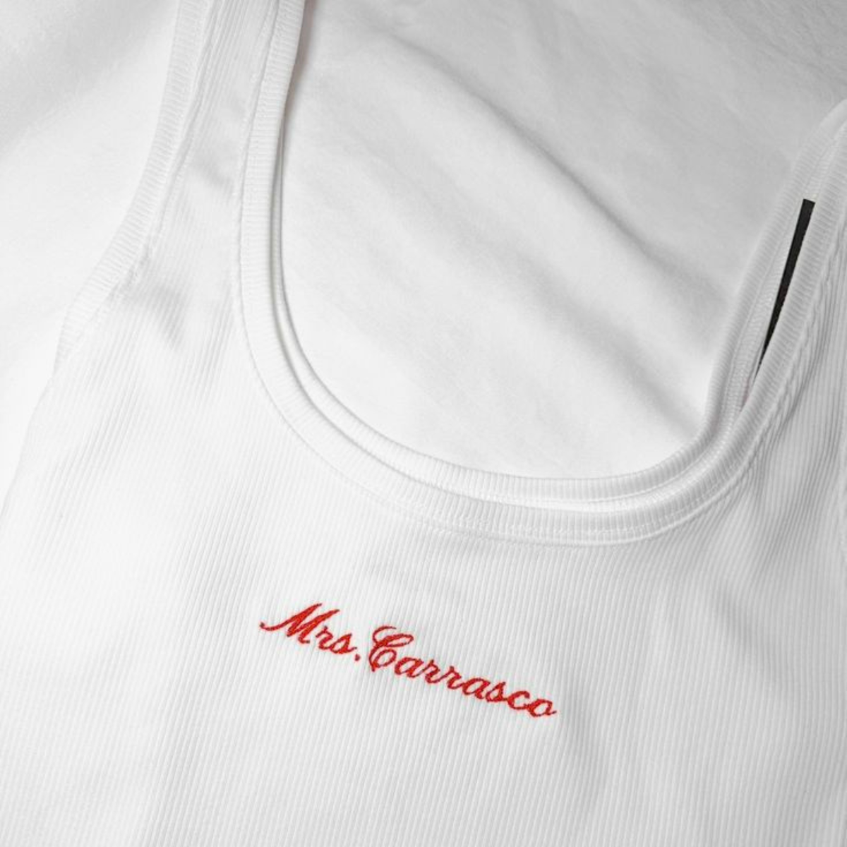 Close-up of a white ribbed tank top with red embroidered 'Mrs. Carrasco' script on the chest.