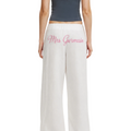 White wide-leg pants with 'Mrs Germain' embroidered in pink script on the back, shown on a model from the back against a light gray studio background.