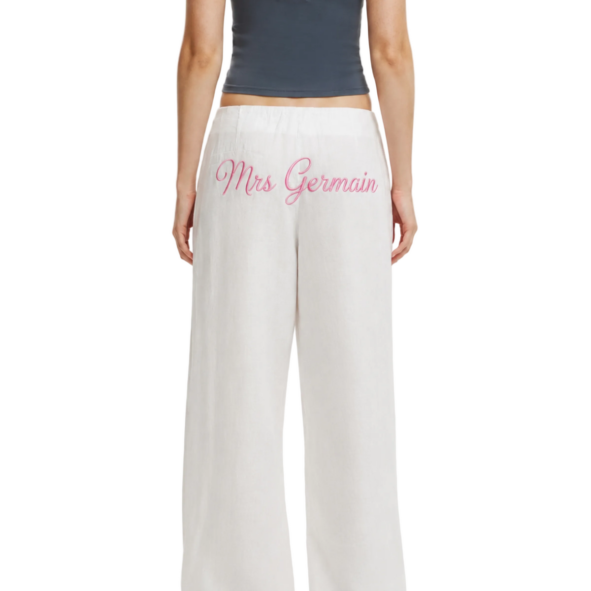 White wide-leg pants with 'Mrs Germain' embroidered in pink script on the back, shown on a model from the back against a light gray studio background.