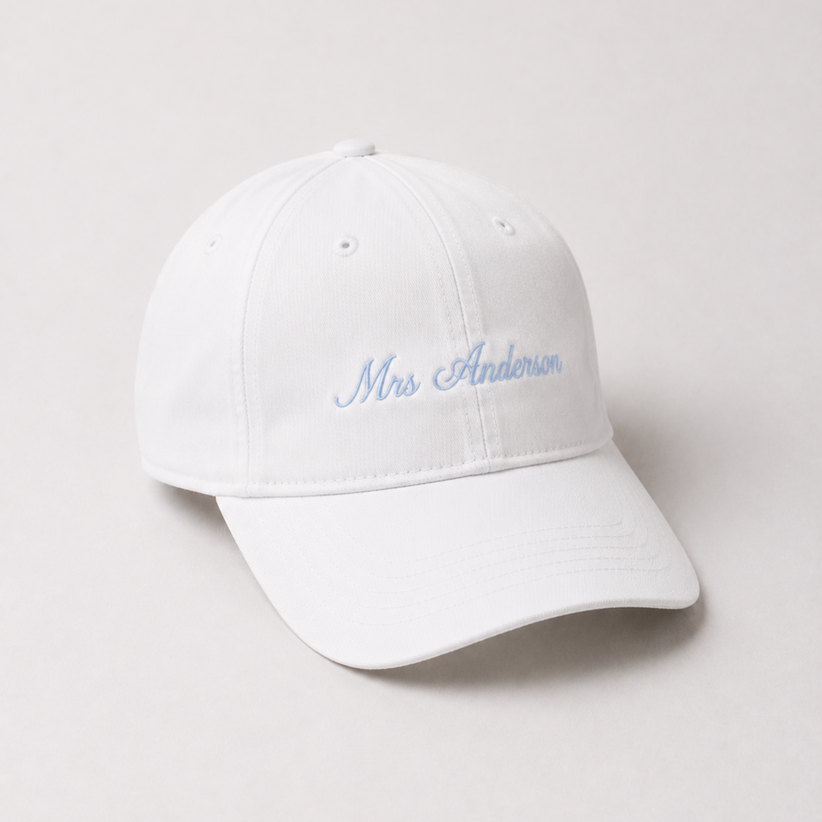 A white baseball cap with 'Mrs Anderson' embroidered in light blue cursive script on the front, shown on a light gray background.