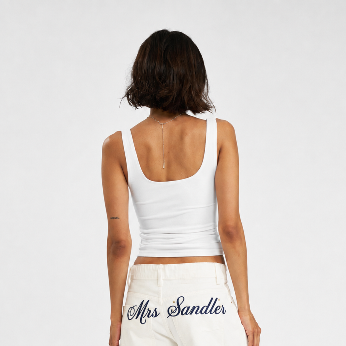 A woman shown from behind wearing a white scoop-neck tank top and white pants with 'Mrs Sandler' embroidered on the back, against a plain light gray background.